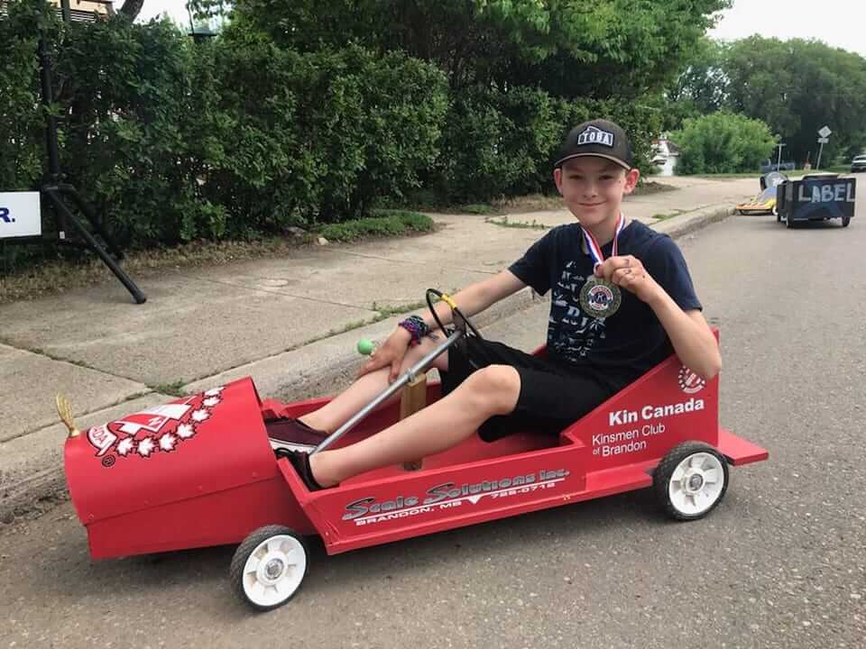 Boy in a Kin Canada box car holding a medal
