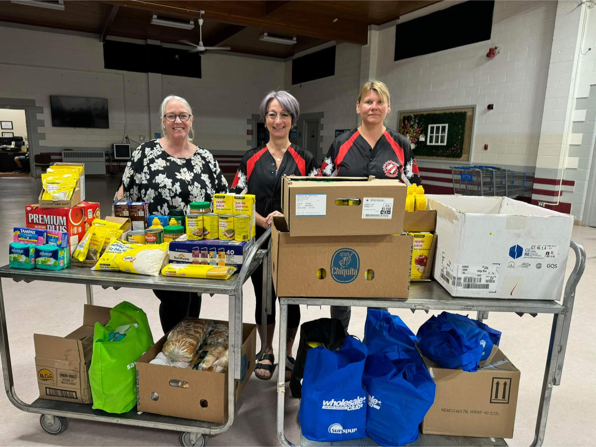 Three Women standing in front of donated food, smiling